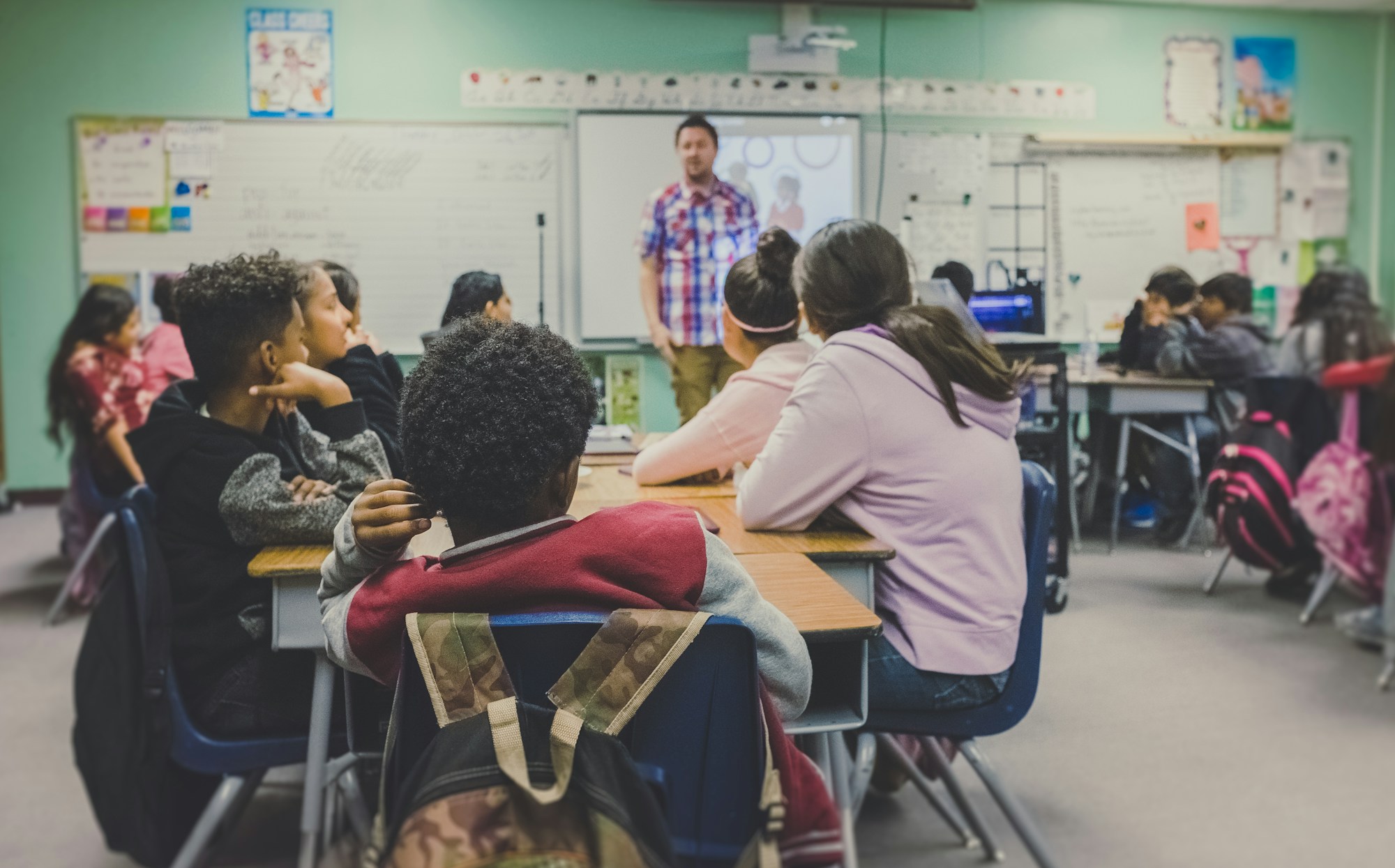 A teacher at a chalkboard with students raising hands